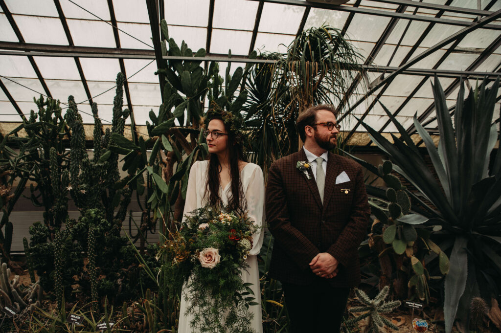 Couple standing in greenery at greenhouse.