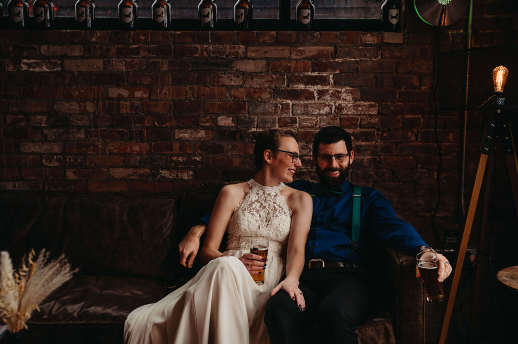 Laid back couple enjoy beers on couch in brick building with boho accents the Chouse.