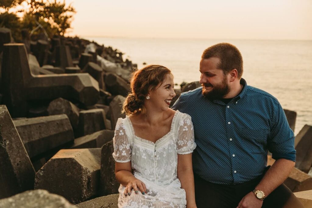 Golden hour at Lakewood Park as couple laughs while sitting on rocks near beach,