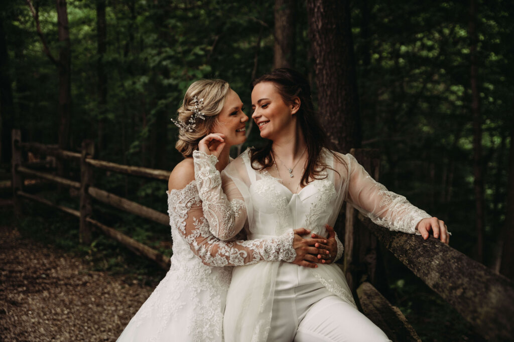 Brides hold each other in the woods on wedding day.