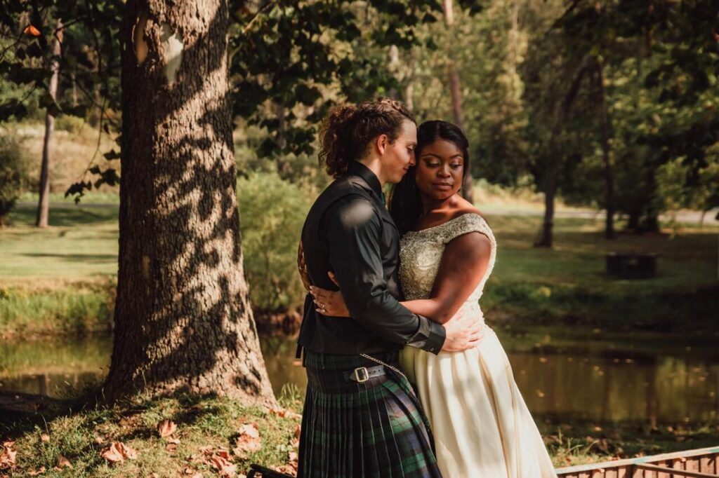 Viking and Native American couple embrace under trees at forest wedding space.