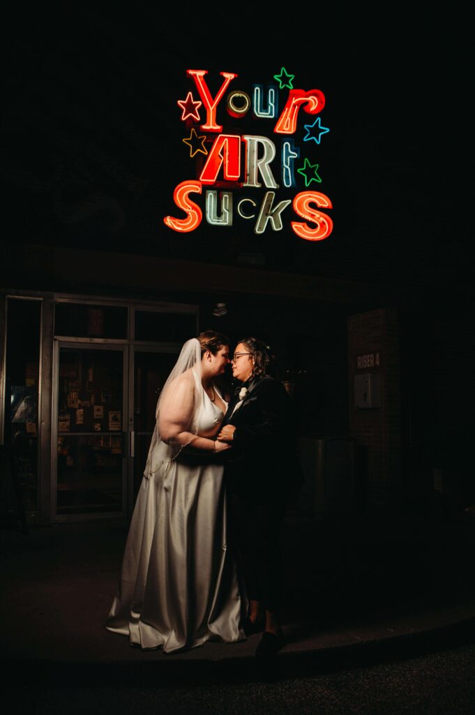 Night photo outside of 78th St STudios with two brides under funny art sign.