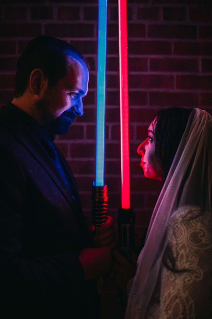 Bride holds red saber across from Groom holding blue saber at night at brewery in Cleveland.