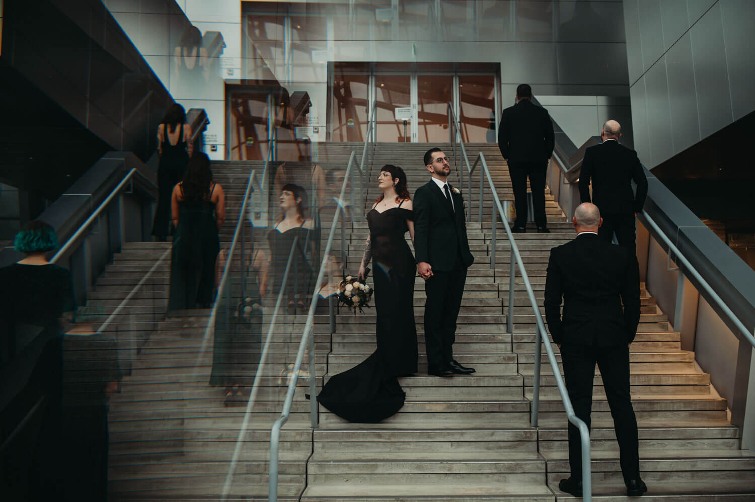 Wedding couple stand on steps with wedding party as a reflection is used to create a unique photo at Akron Art Museum.
