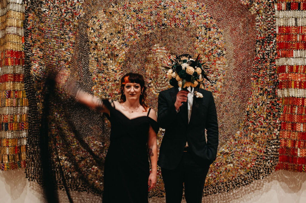 Unique and non tradtional wedding photo at art musuem in front of an exhibit.