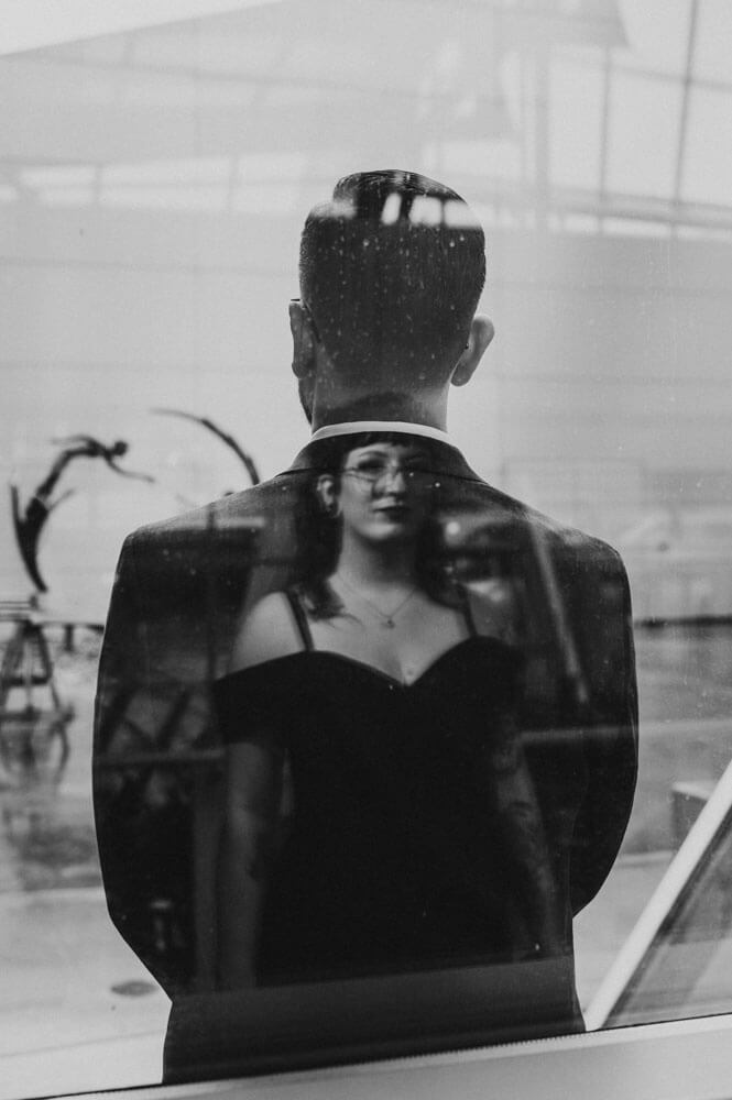 Black and white unique wedding photo of bride posed into groom's figure using a window of museum.