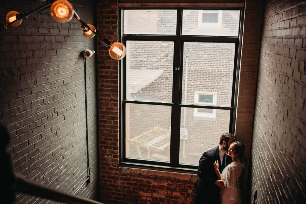 Couple cuddle up in a industrial hallway with brick and warm lighting. 