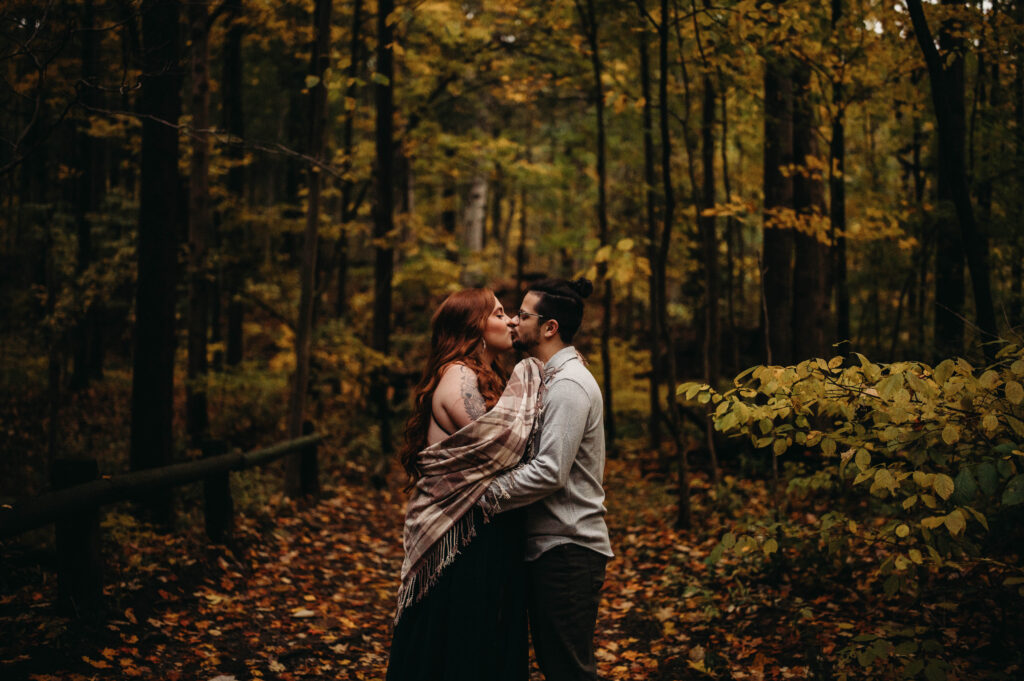 Couple elopes in fall forest and kiss amoung the colorful leaves.