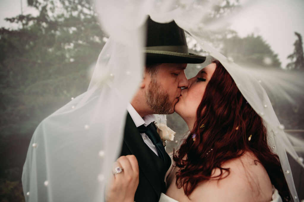 Newlyweds kiss under pear veil while Bride wears flowers in her hair.