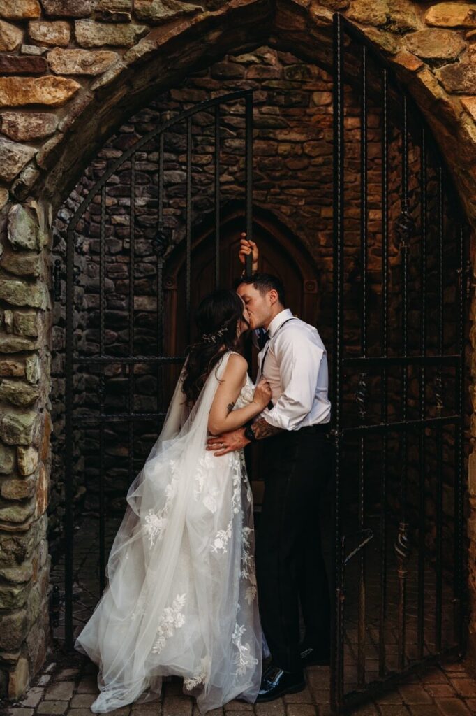 Married couple kiss in front of castle gates in Scotland.