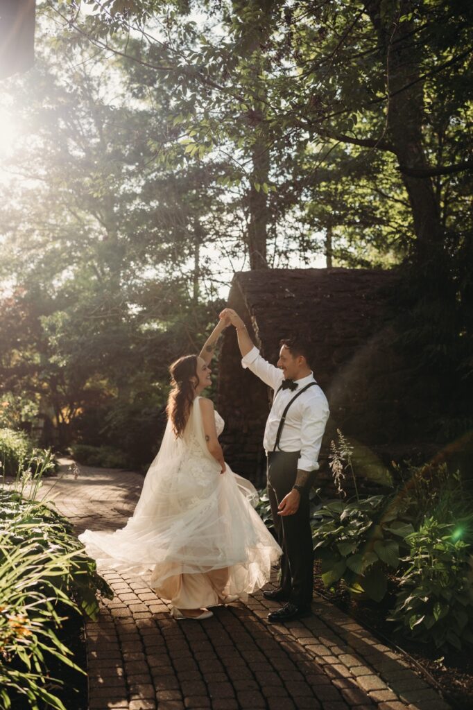 SUn kisses edge of image as groom twirls his bride in garden path