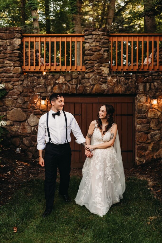 Newlyweds walk from brick facade at golden hour.