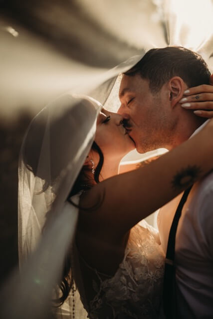 Couple kiss under veil creating a magical glowy light for their whimsical day.