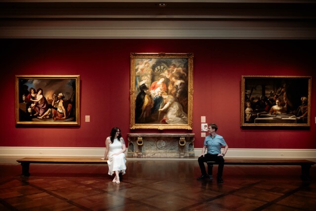 Couple sits on benches at art museum for engagement session.