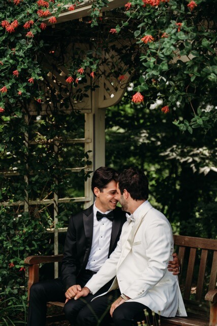 Couple sit beneath floral and greenery in garden