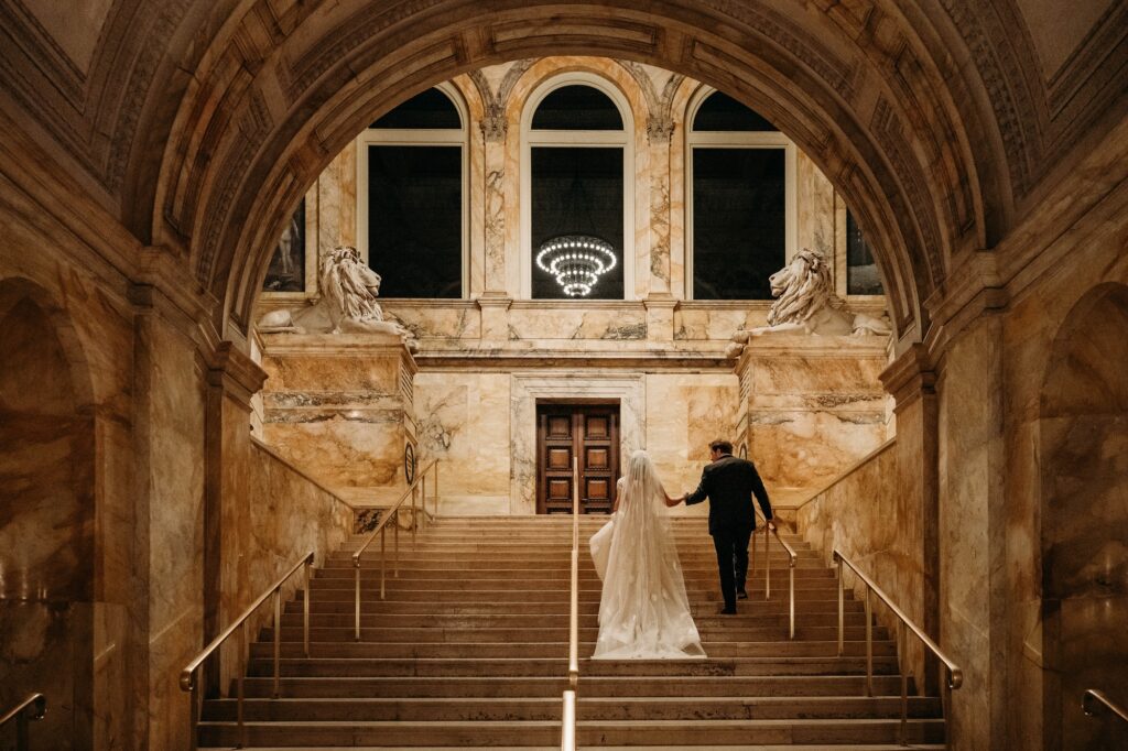 Wedding couple walk up grand stair case at Boston Public Library in evening.